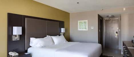 A hotel room with a large bed, a bedside table with a lamp, a phone, and a door leading to a bathroom.