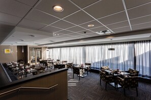 Eine Hotelhalle mit einer Rezeption, einer Sitzecke und großen Fenstern mit Vorhängen.