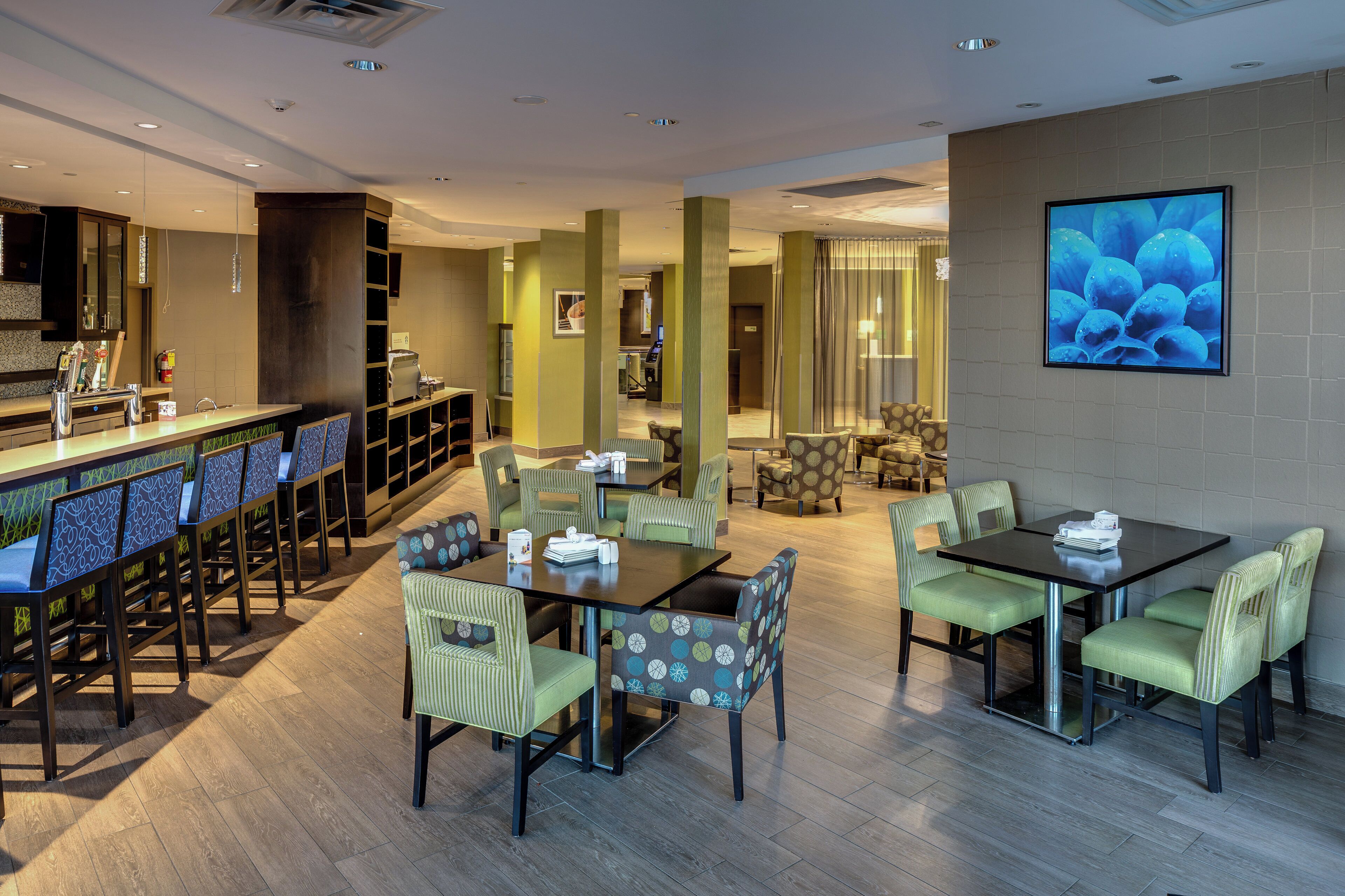 A hotel lobby with a bar area, seating arrangements, and a large screen displaying an image.