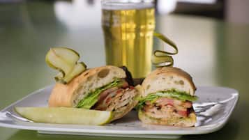 A sandwich cut in half with pickles on a plate, a glass of beer, and a table.