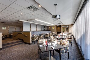 Een restaurantgedeelte in een hotel met meerdere tafels en stoelen, een bar in het midden en een trap naar een hoger niveau.