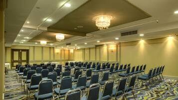 A conference room with rows of chairs, a patterned carpet, and chandeliers.