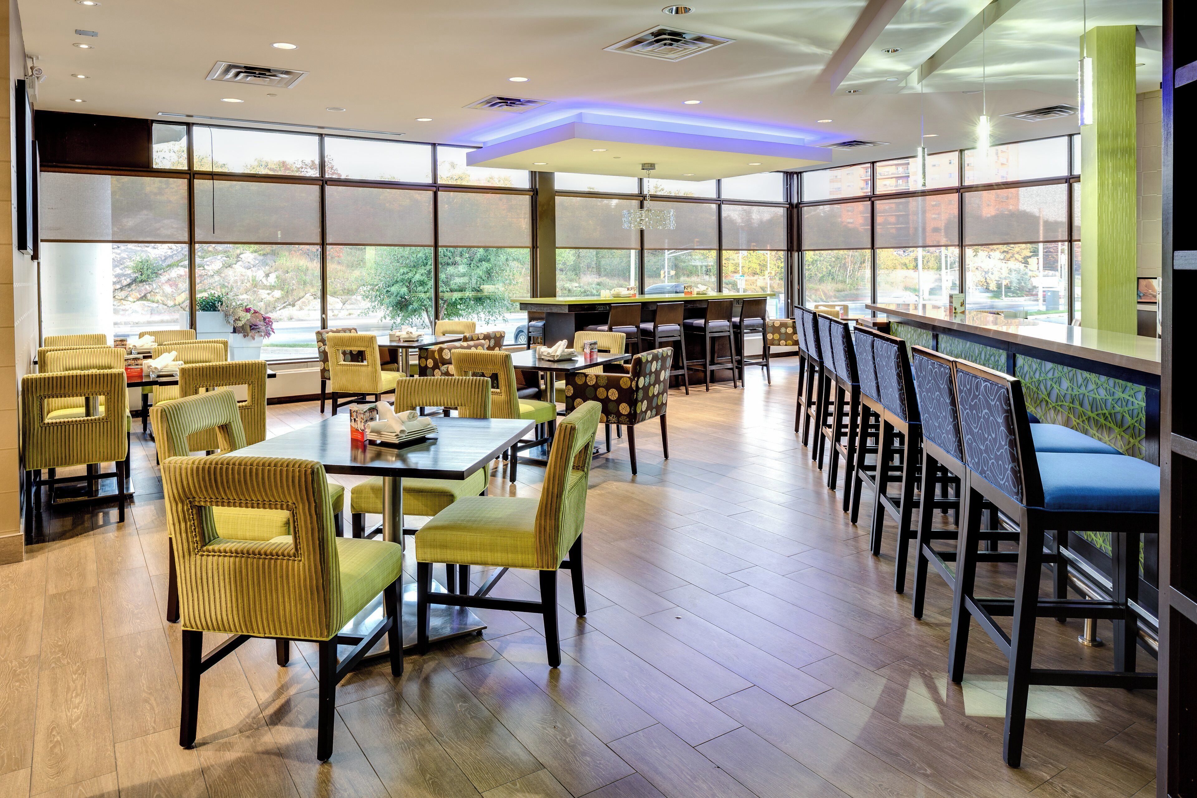 A restaurant with multiple tables and chairs, large windows, and a modern ceiling design.