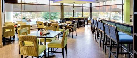 A restaurant with multiple tables and chairs, large windows, and a modern ceiling design.