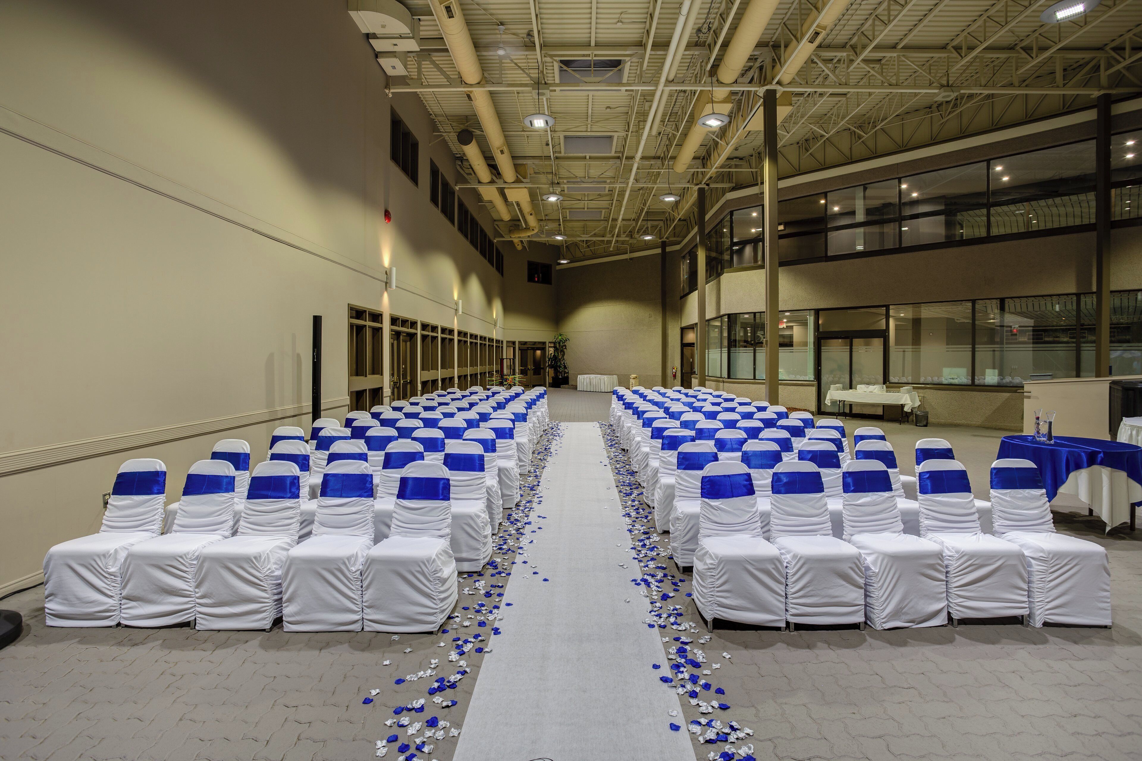 A large indoor hall with rows of chairs covered in white and blue sashes, arranged for an event.