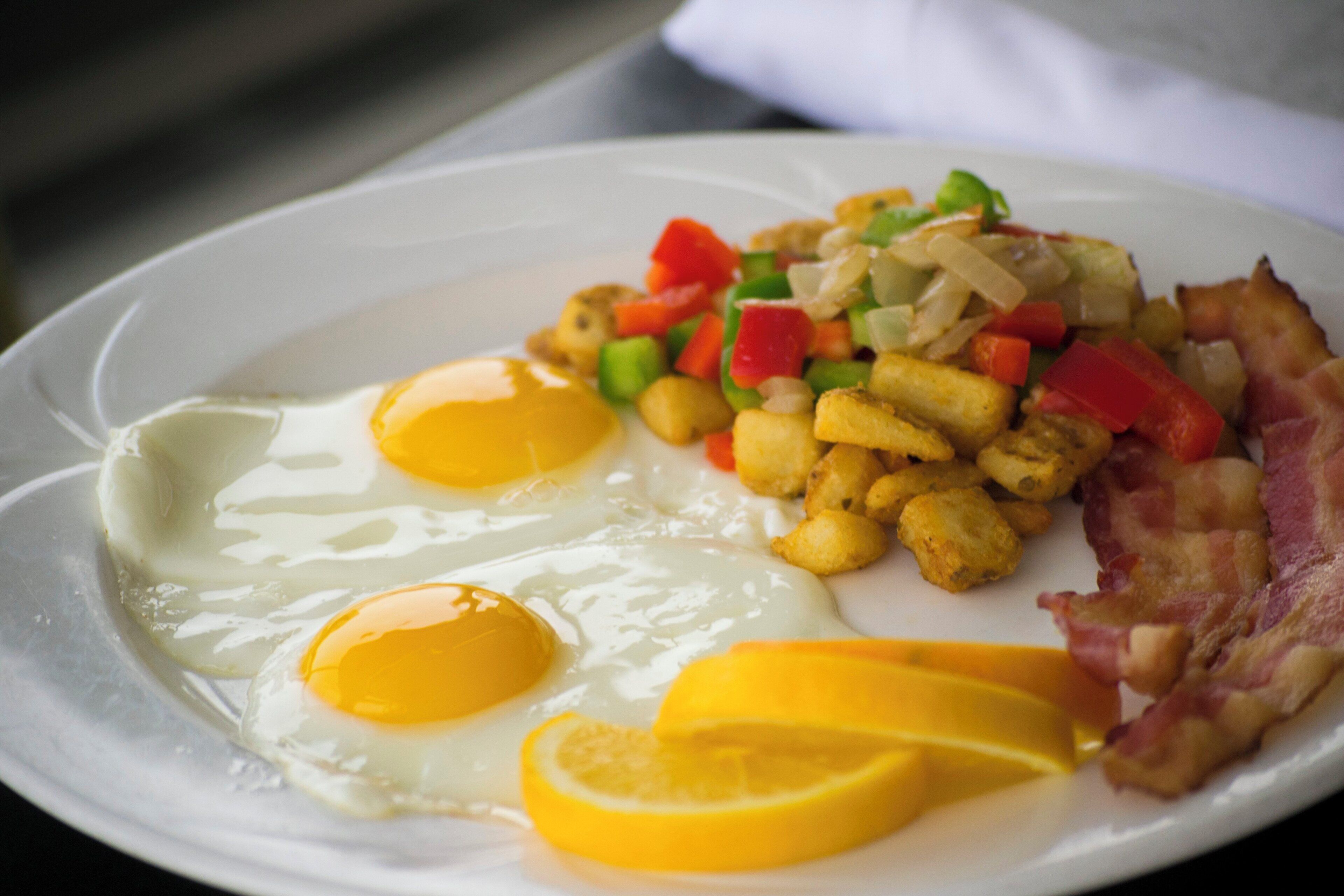 A plate with eggs, bacon, diced vegetables, and orange slices.