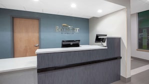 A reception desk with a blue wall, a wooden door, and a black monitor. - Baymont Inn & Suites Grand Rapids Near Downtown (Grand Rapids)