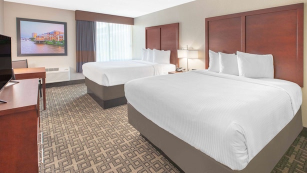 A hotel room with two beds, a desk, a TV, and a large window with curtains. - Baymont Inn & Suites Grand Rapids Near Downtown (Grand Rapids)