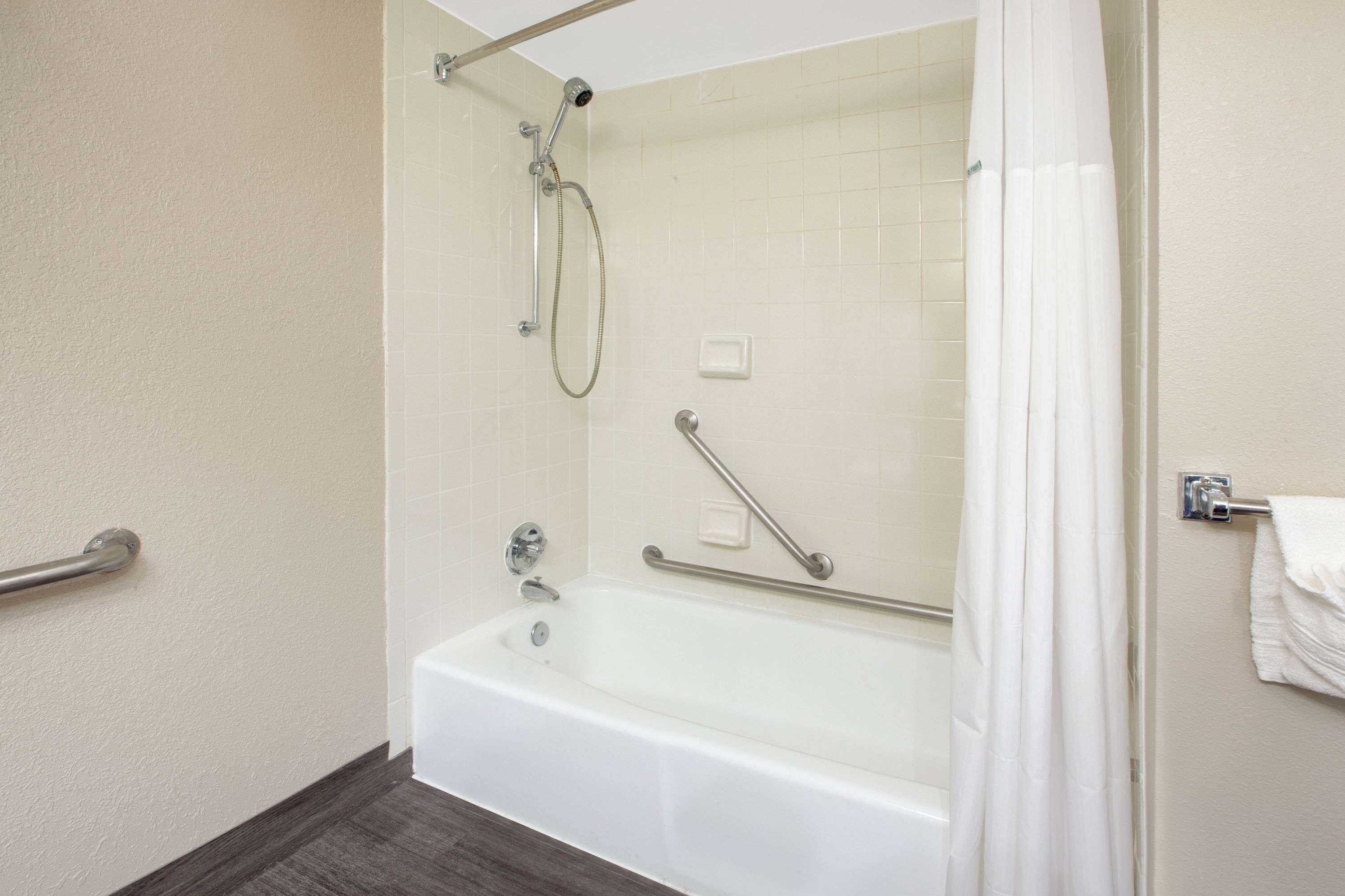 A bathroom with a bathtub, a shower, and a handrail.