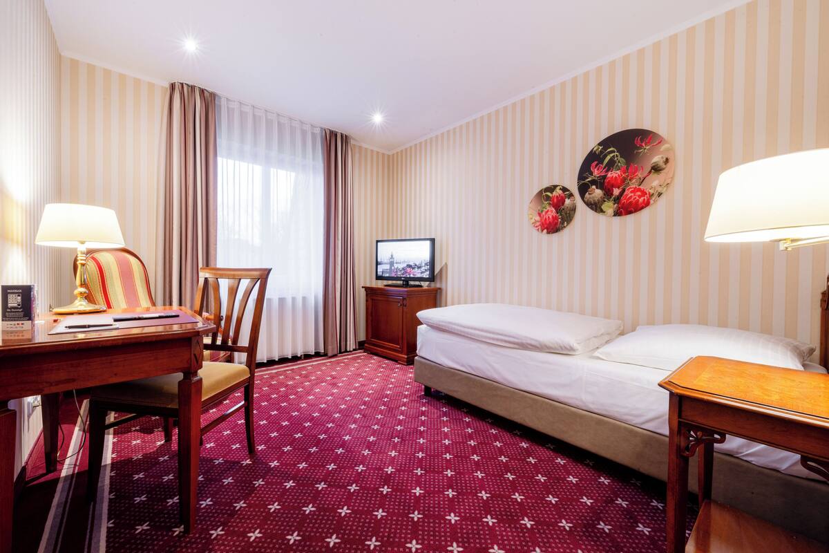 A hotel room with a bed, a desk, a chair, a television, and a decorative wall piece.