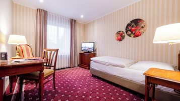 Una habitación de hotel con cama, escritorio, silla, televisor y un adorno en la pared.