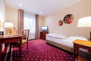 Ein Hotelzimmer mit Bett, Schreibtisch, Stuhl, Fernseher und einer Wanddekoration.