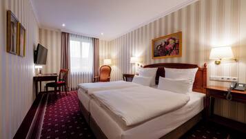 A hotel room with two beds, a desk, a chair, a TV, and a painting on the wall.