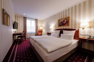 Ein Hotelzimmer mit zwei Betten, einem Schreibtisch, einem Sessel, einem Fernseher und einem Bild an der Wand.