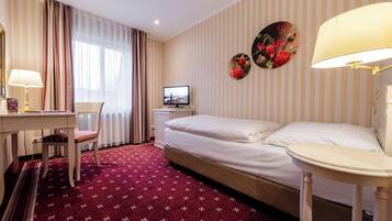 Una habitación de hotel con cama, escritorio, silla, televisor y lámpara.