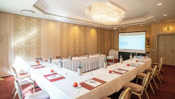 A conference room with a long table, chairs, a projector screen, and a chandelier.