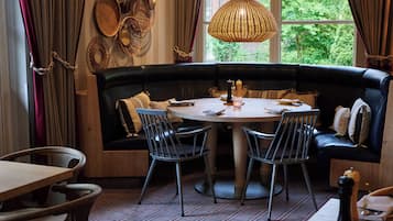 Un rincón comedor acogedor con una mesa redonda, un banco de cuero negro y decoración de mimbre en la pared.