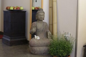 Una statua raffigura una figura seduta con un fiore in grembo, una pianta in vaso e un mobile con delle mele.