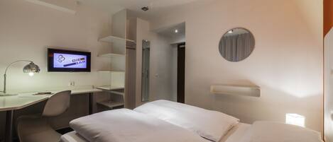 Habitación de hotel moderna con una cama, un escritorio y un televisor mostrando 'Die Bar'.