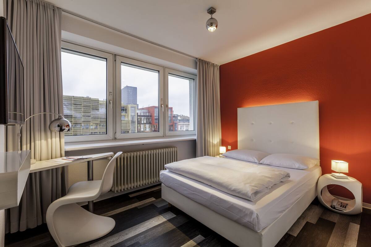 A modern hotel room with a large bed, a desk, and a chair.