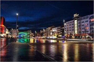 Ein beleuchtetes Stadtbild bei Nacht, mit dem Hotel "Hotel Monopol" deutlich sichtbar auf der rechten Seite.