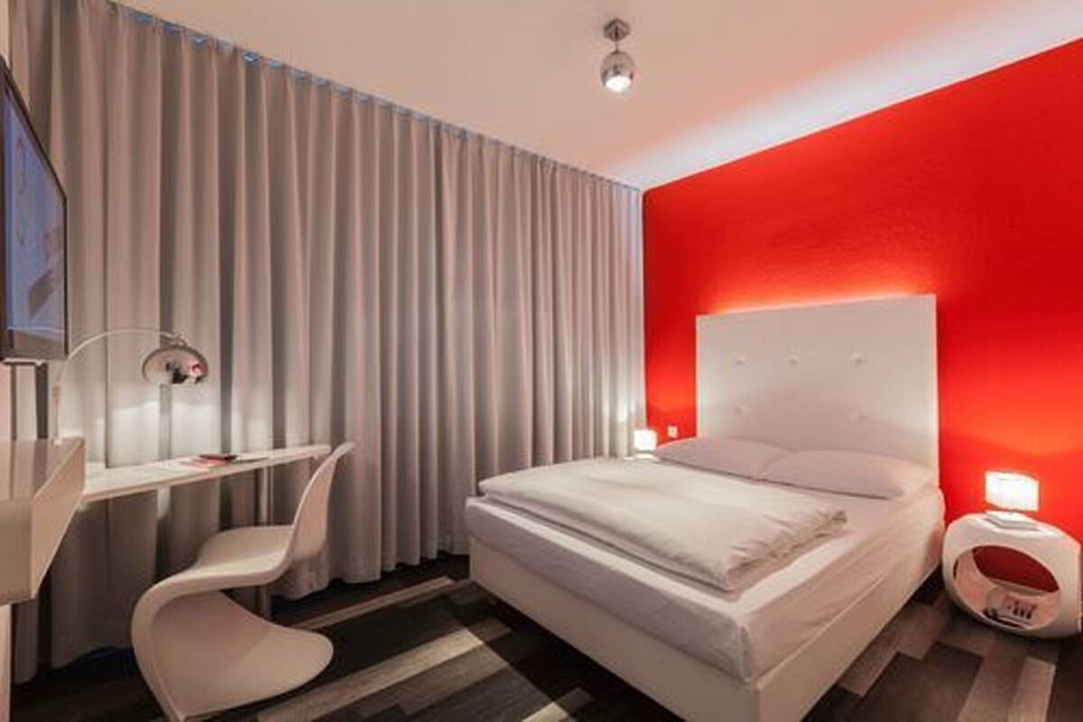 A modern hotel room with a bed, a desk, and a chair.