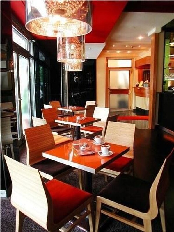 Un café moderne avec des tables et des chaises en bois, un grand lustre et une vue sur la rue.