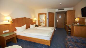A hotel room with a double bed, a desk with a chair, a small table, and a TV mounted on the wall.