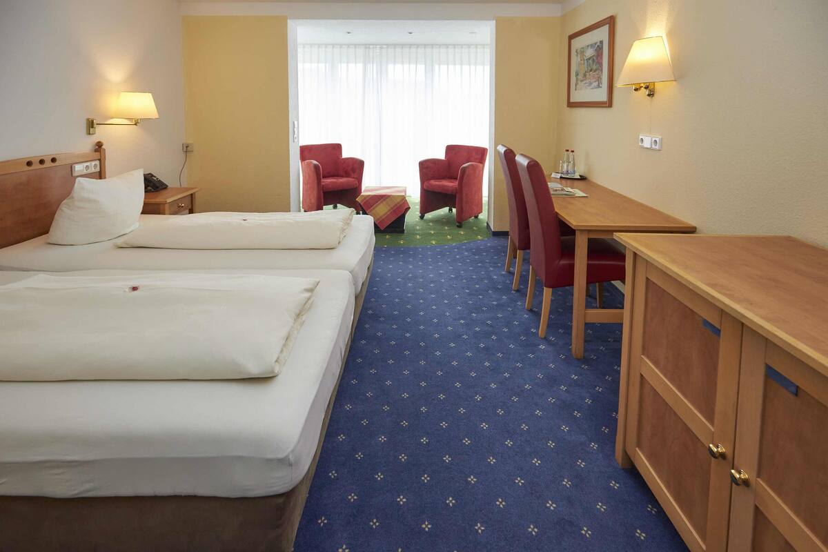 A hotel room with two beds, a desk, chairs, and a small table.