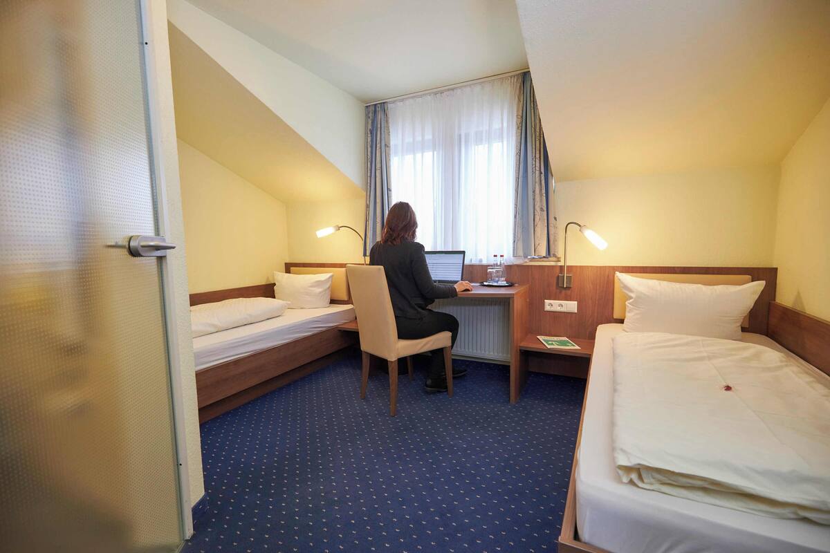 A hotel room with two single beds, a desk with a computer, and a chair.