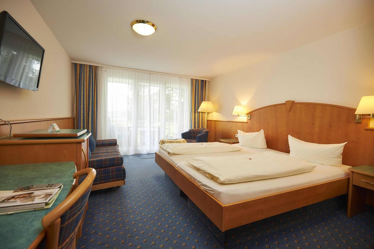 A hotel room with a large bed, a desk with a chair, a television, and a window with curtains.