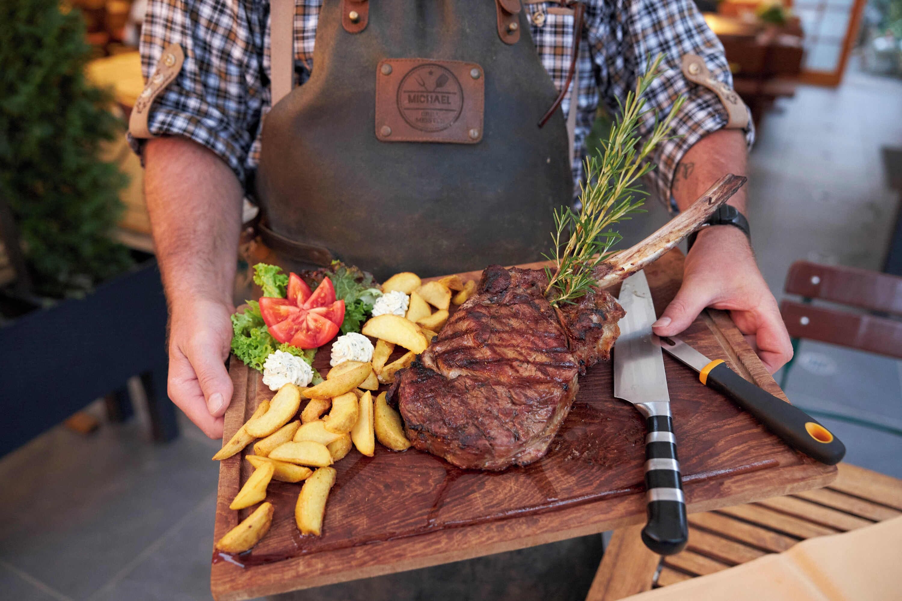 Une personne tenant une planche à découper en bois sur laquelle se trouvent un steak, des frites et des légumes.