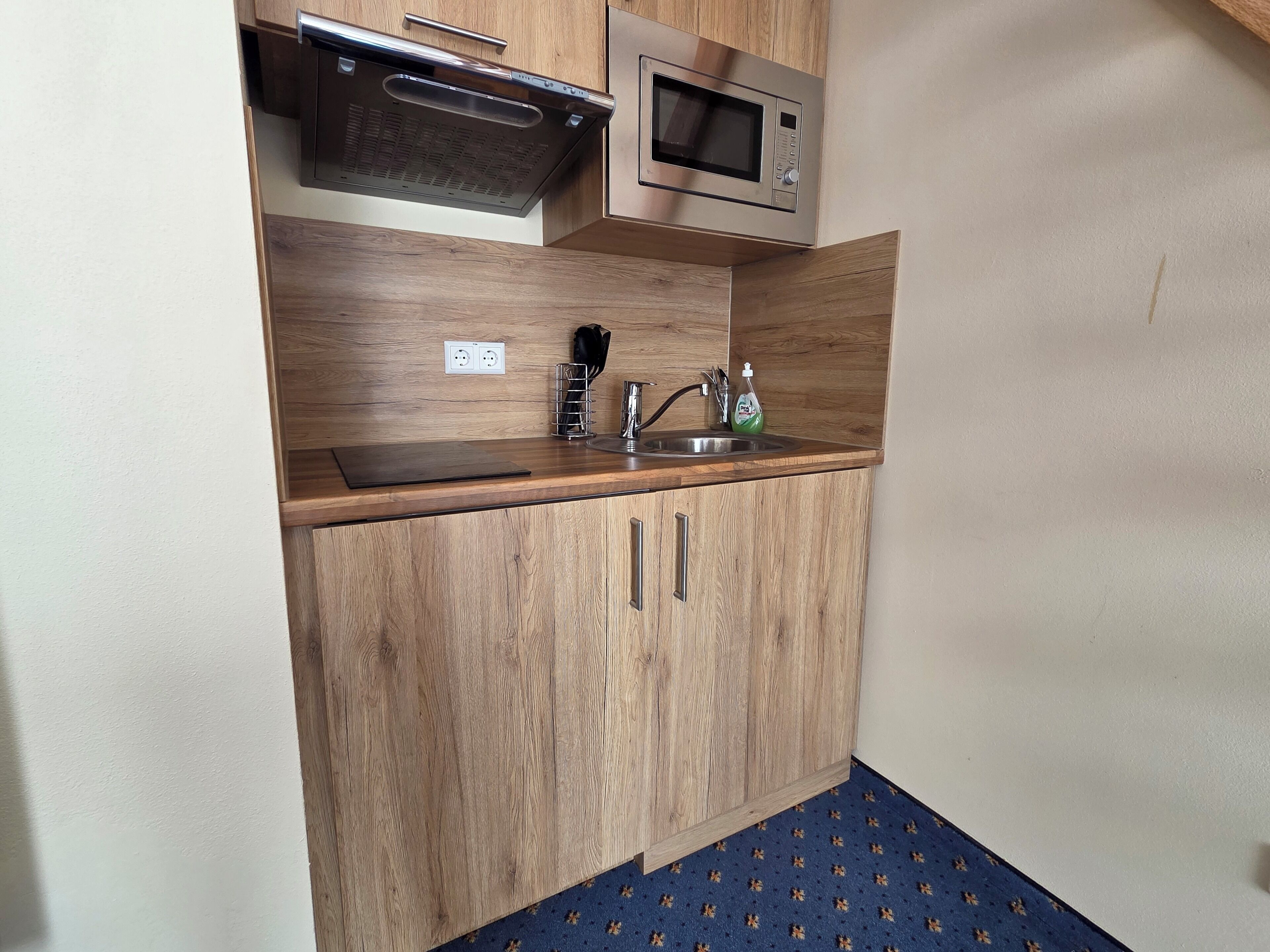 A compact kitchen with wooden cabinets, a stainless steel microwave, and a sink.