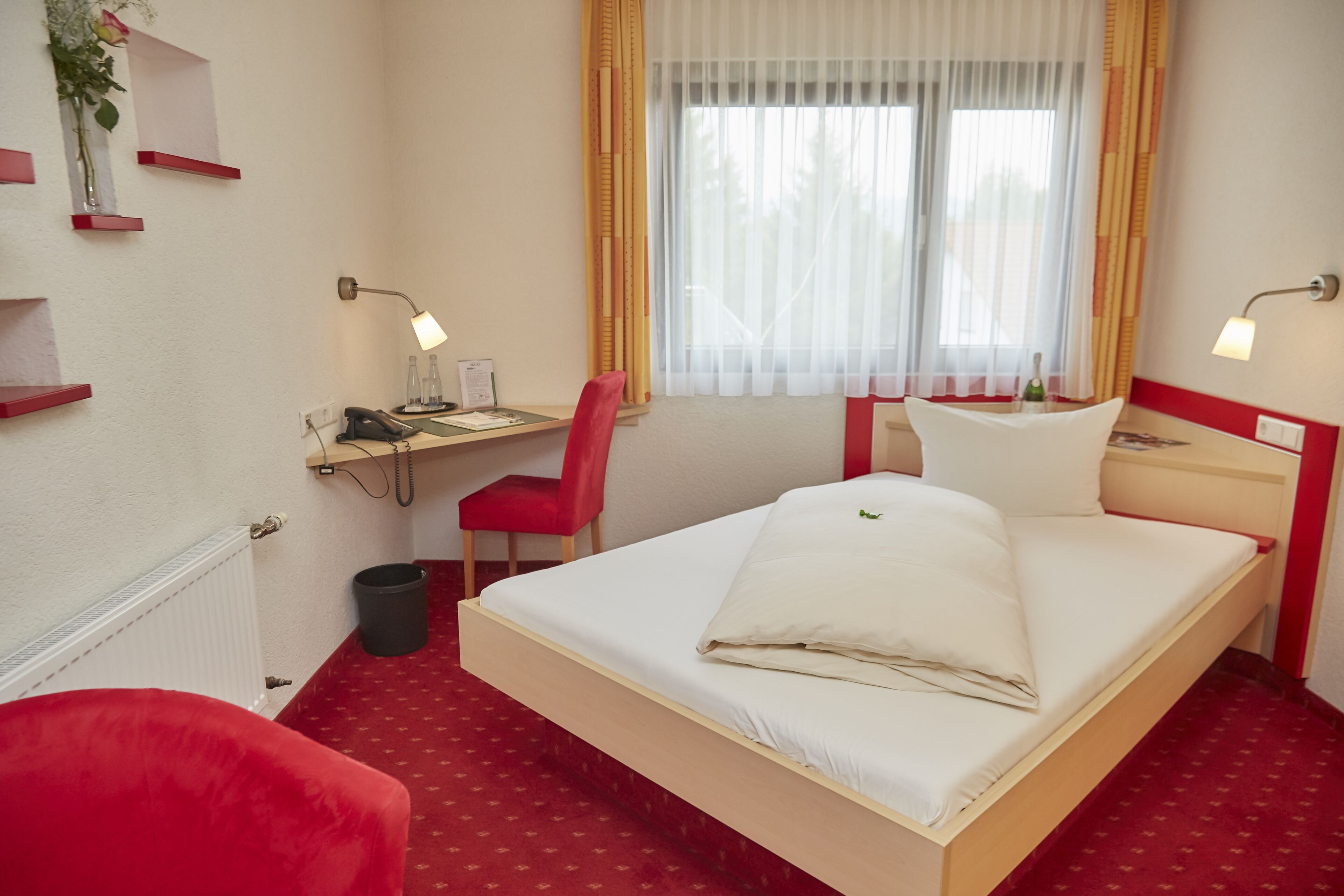 Habitación de hotel con una cama individual, un escritorio con silla, un teléfono y una ventana con cortinas.