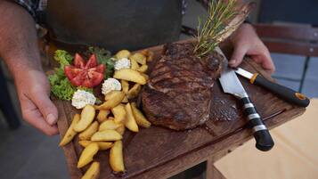 A person holding a wooden board with a steak, fries, and a garnish.