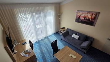 A hotel room with a dining table, a sofa, a painting, and a floor lamp.
