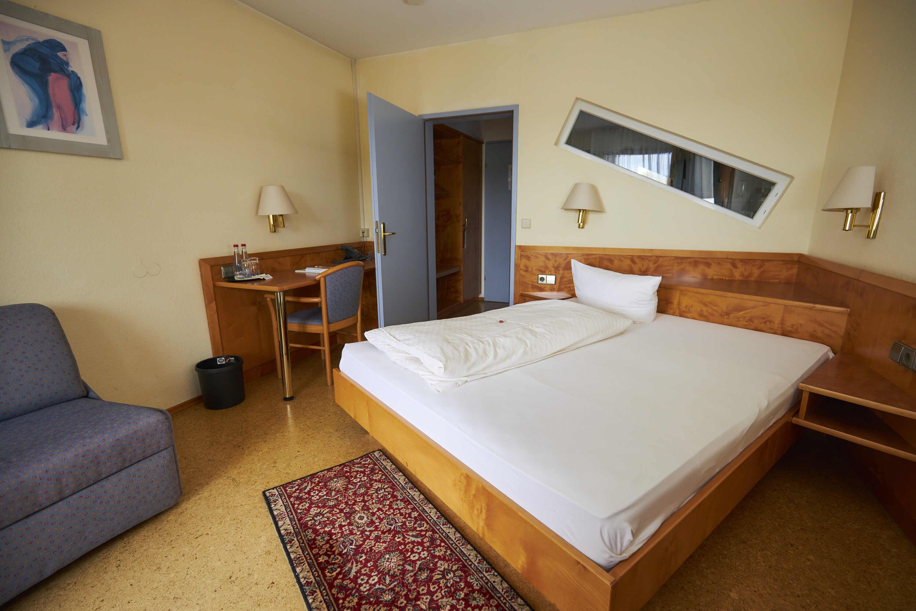 A hotel room with a bed, a desk, a chair, a small table, and a nightstand.
