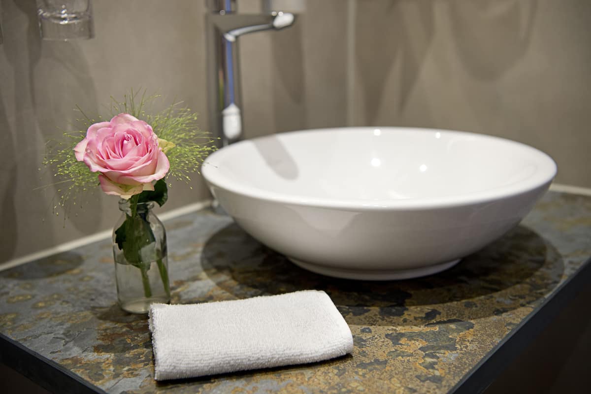 Ein Waschbecken mit Blumen in einer Vase und einem weißen Handtuch auf einer Granitplatte.