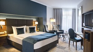 A hotel room with a large bed, two armchairs, a small table, a TV, and a desk with a computer. - Hotel Schwarzer Bär (Jena)