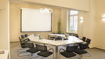 A conference room with a large table, black chairs, a projector screen, and a plant.