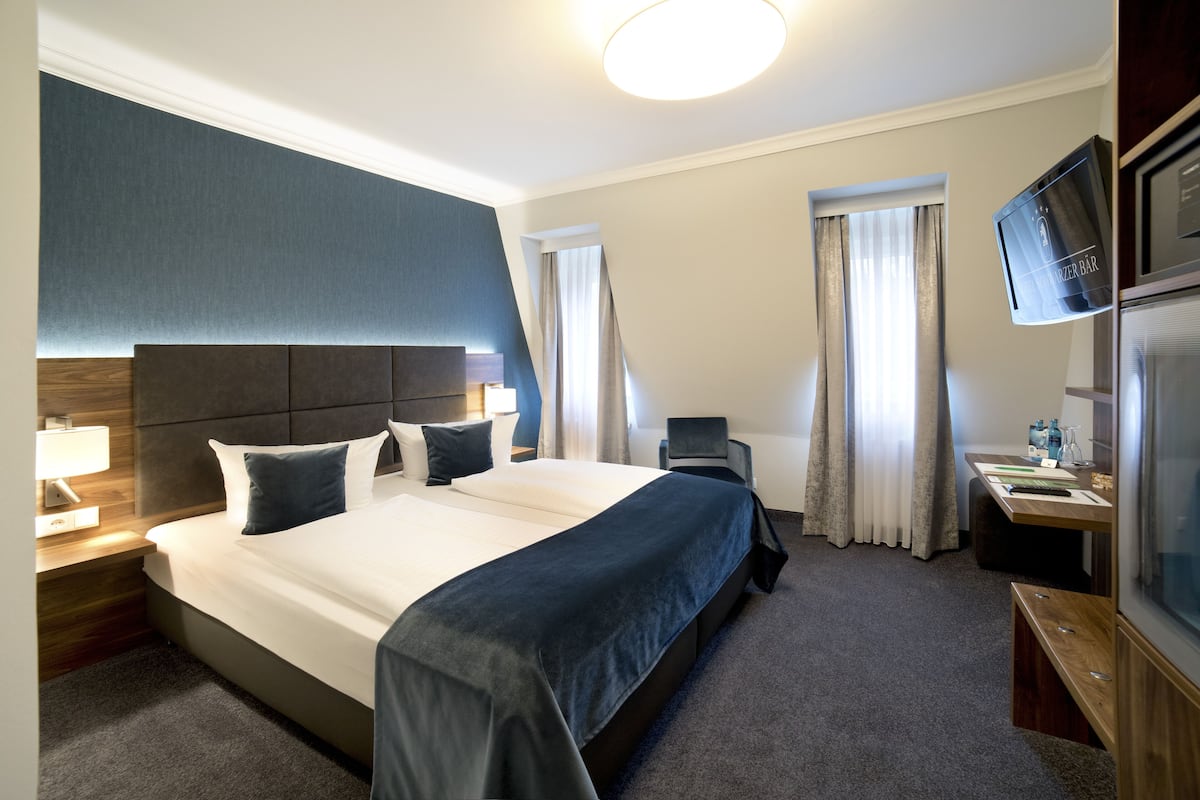 Ein Hotelzimmer mit einem großen Bett, einem Schreibtisch, einem Fernseher und einem Fenster mit Vorhängen.