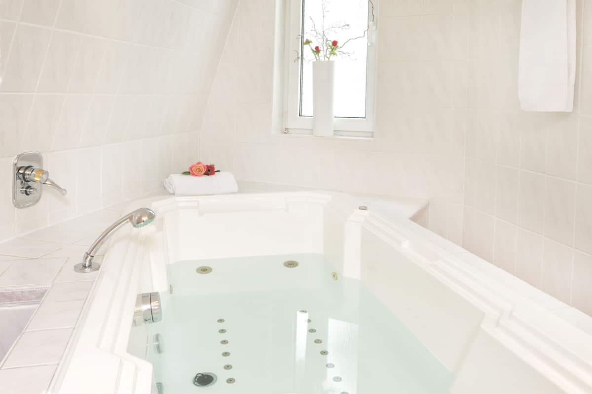 Ein modernes Badezimmer mit einer Glaskabine zur Badewanne, einem Fenster mit Ausblick und einem weißen Handtuch am Rand.