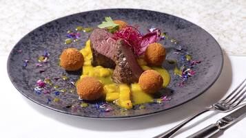 Un plato de comida con un trozo de carne, dos elementos redondos y una guarnición sobre un plato oscuro.