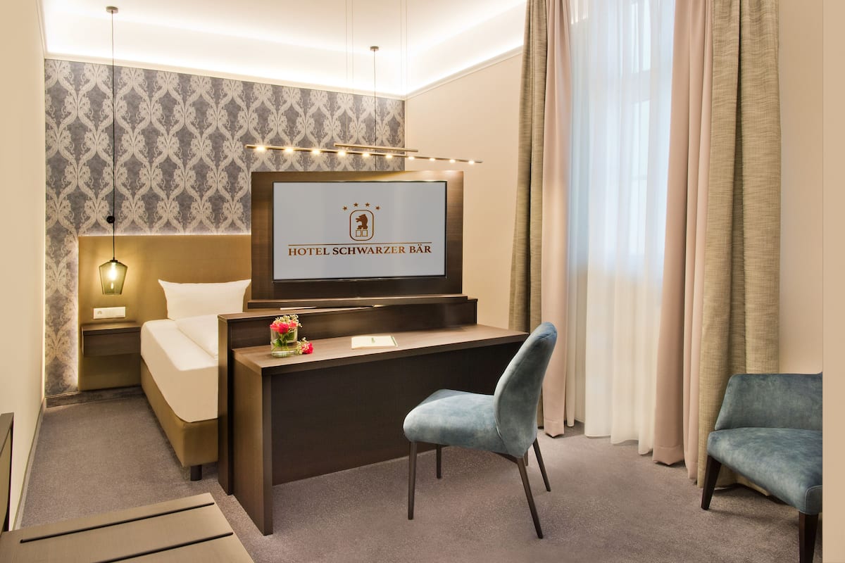 Ein Hotelzimmer mit Bett, Schreibtisch mit Fernseher, der den Hotelnamen anzeigt, einem Sessel und einer Couch.