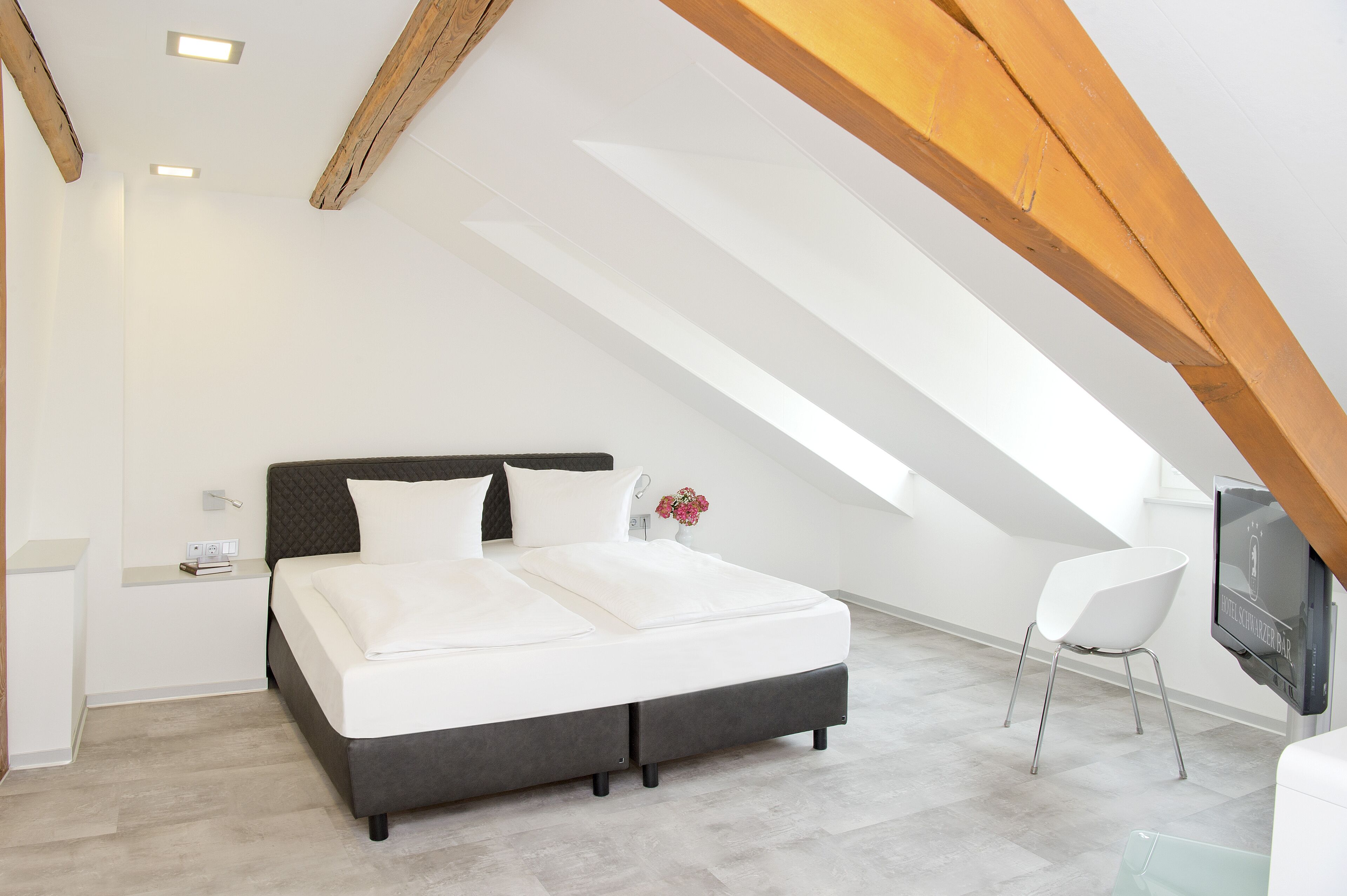 A modern bedroom with a large bed, a white chair, and a TV mounted on the wall.