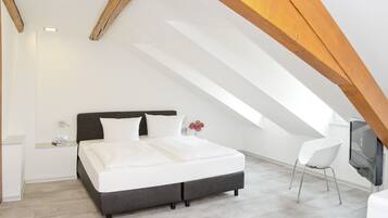 A modern bedroom with a large bed, a white chair, and a TV mounted on the wall.