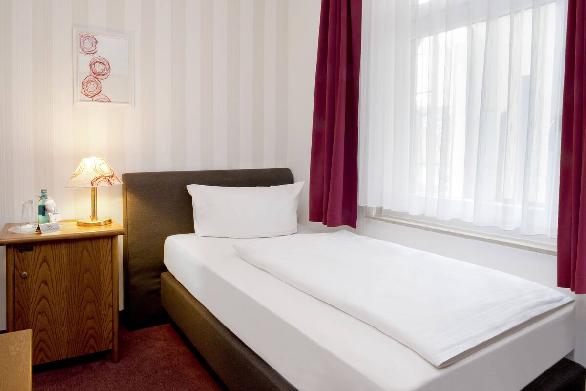 Ein Hotelzimmer mit Bett, Nachttisch mit Lampe und einem Vorhangfenster.