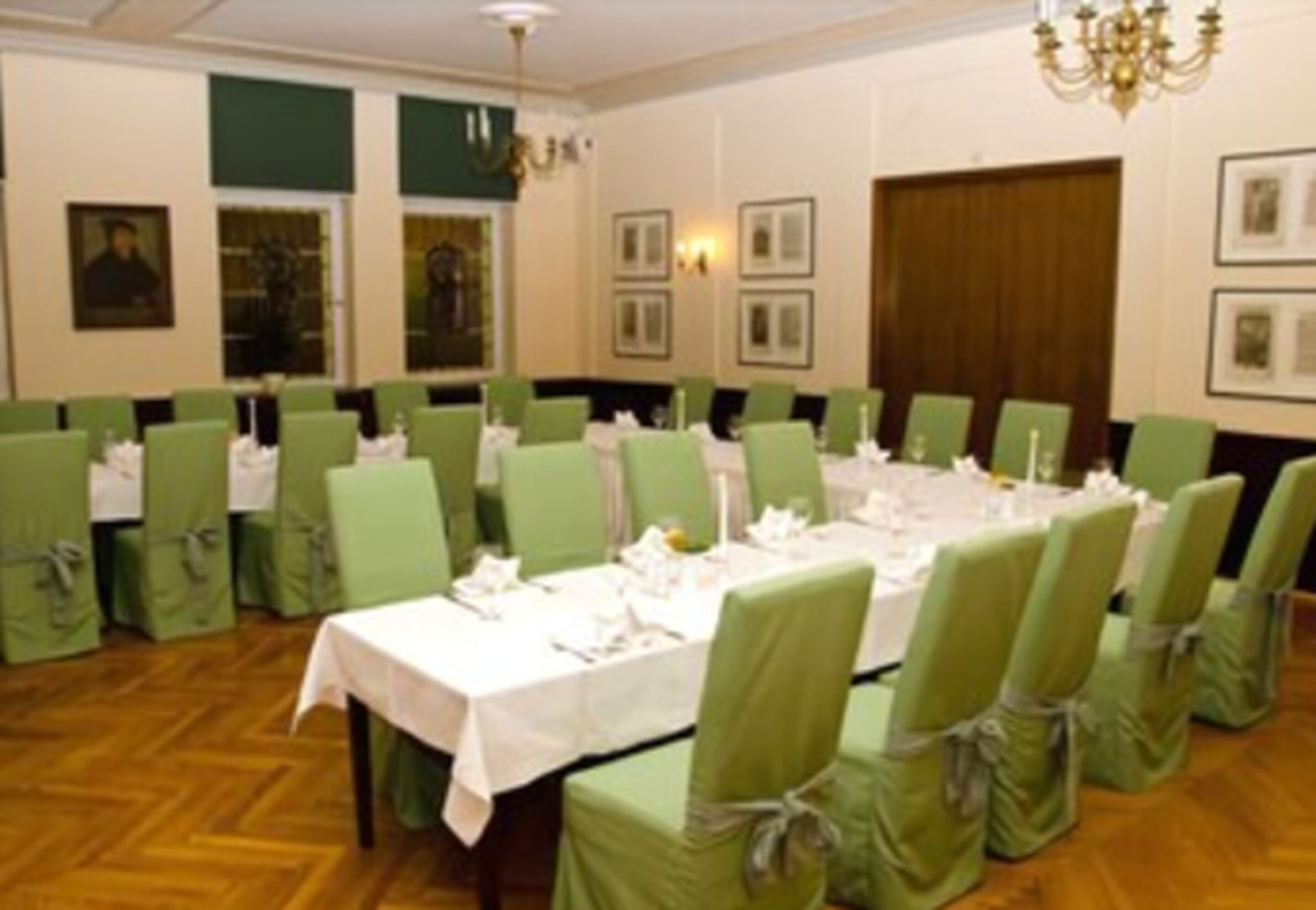 A conference room with green chairs, white tablecloths, and framed pictures on the walls.