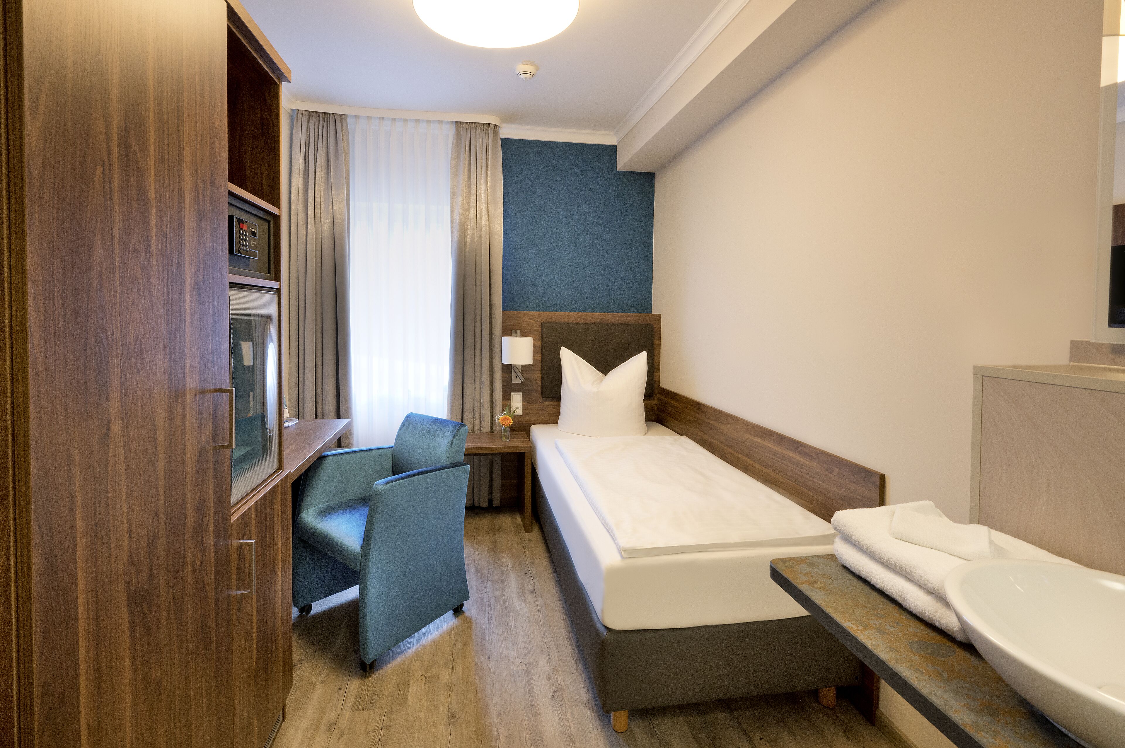 A hotel room with a bed, a desk, a chair, a TV, and a bathroom with a sink and toilet.
