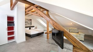 A modern hotel room with a sloped ceiling, a wooden staircase, a bed, a sofa, and a red storage unit. - Hotel Schwarzer Bär (Jena)